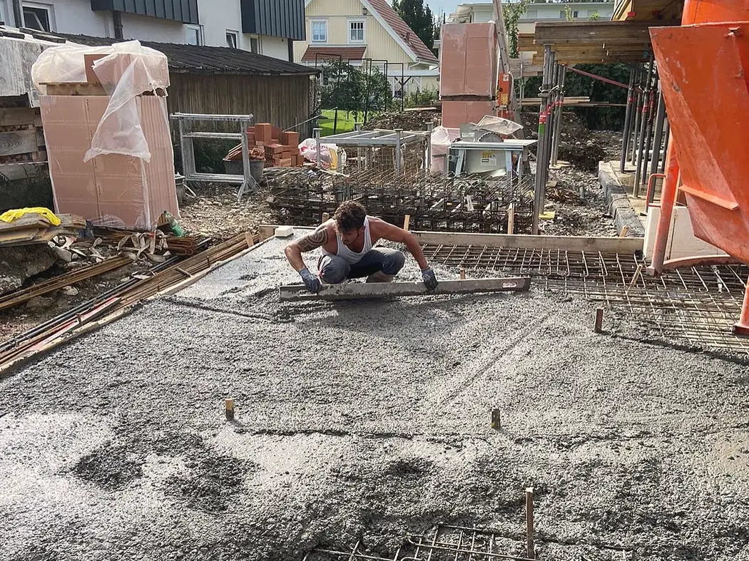 Deniz zieht auf einer Rohbaustelle die frisch betonierte Bodenplatte ab