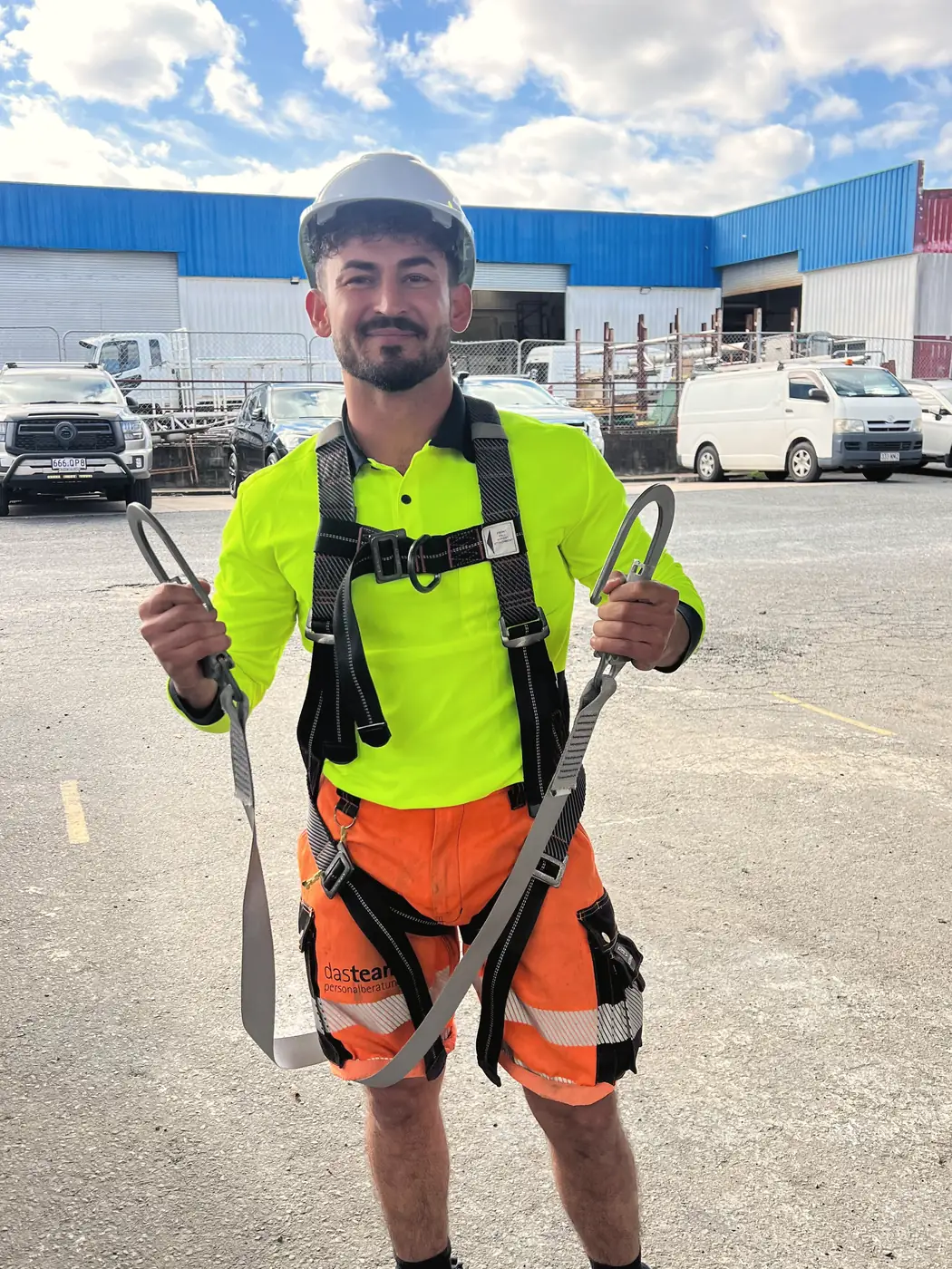 Deniz in Warnkleidung mit Auffanggurt auf einem Betriebshof in Australien