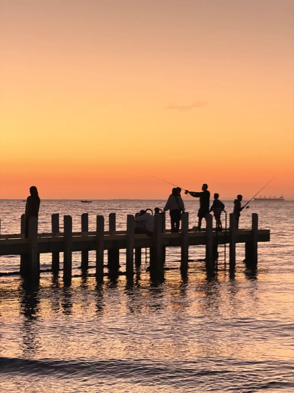 Menschen als Silhouetten auf einem Holzsteg im Wasser bei Sonnenuntergang